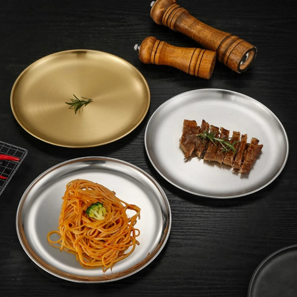 a three stainless steel round plates of food on a table and wooden pepper grinders