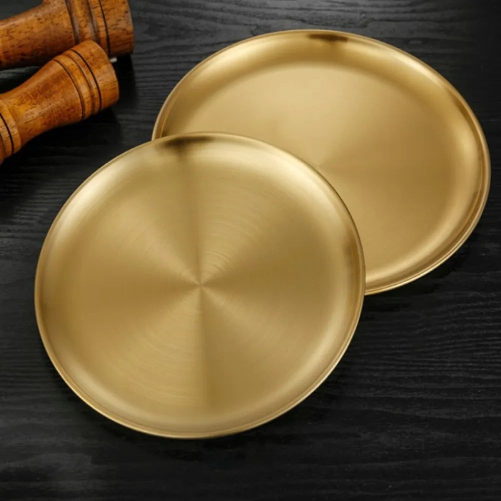 two gold stainless steel round plates and wooden pepper grinders